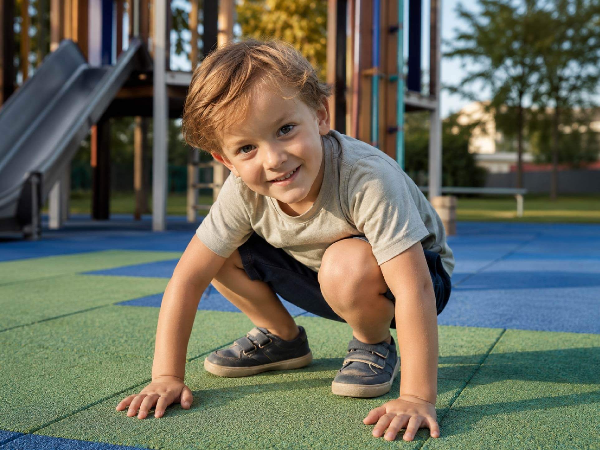 Kind hockt auf Fallschutzplatten auf dem Spielplatz