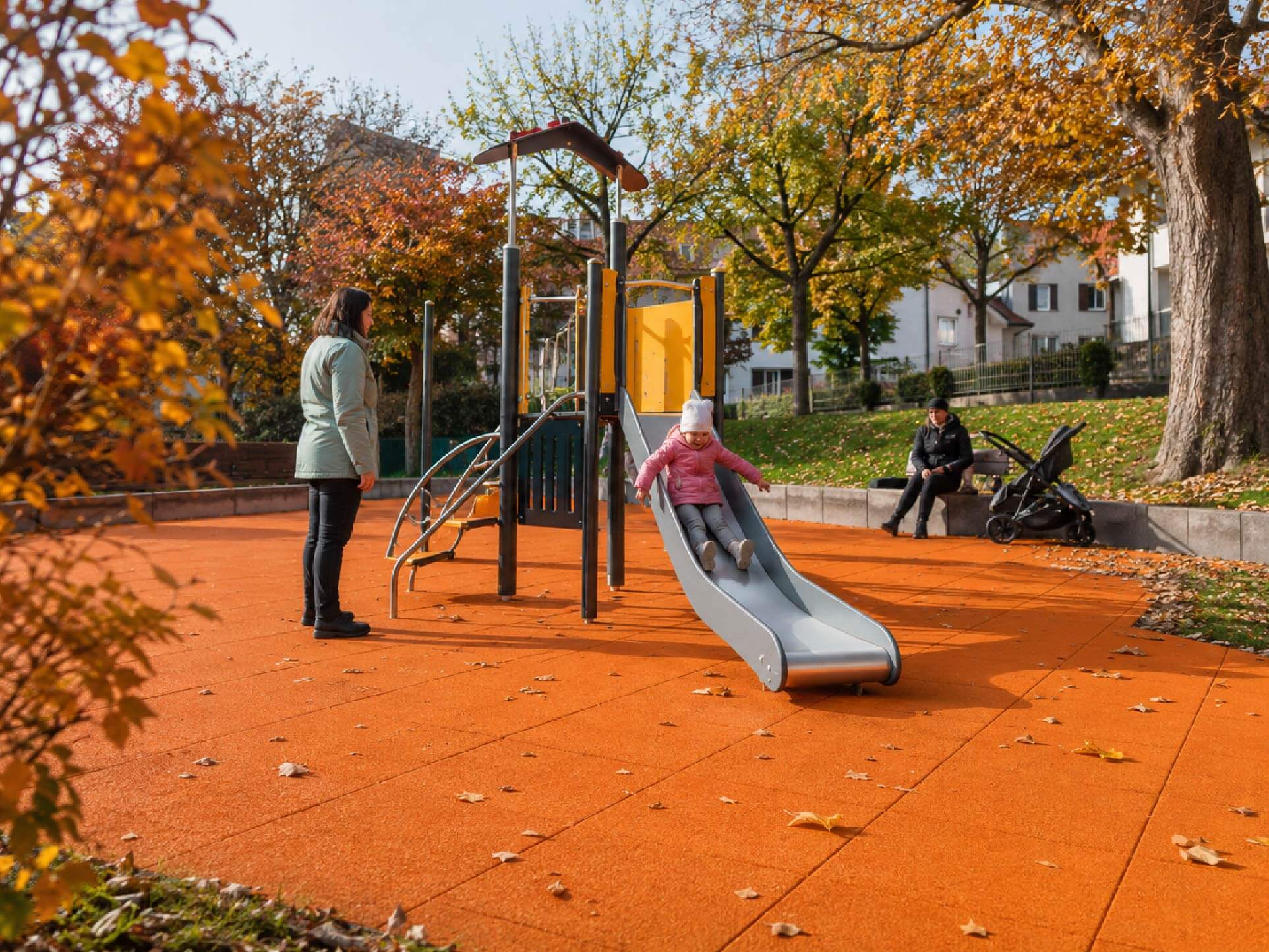Rutschendes Kind mit Erwachsenen auf dem Spielplatz im Herbst